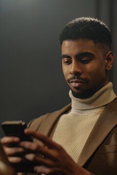 Young man using smartphone messaging in brown turtleneck