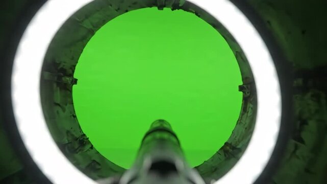 Digital borescope camera POV gliding through a dark industrial metallic pipe towards a bright green screen background for chroma key compositing