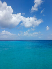 Fototapeta premium Tropical seascape with turquoise water and blue sky with clouds. Minimalist view of the open sea on a bright sunny day. Vertical background for travel and vacation concepts 