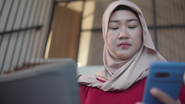 Close-up of a Muslim woman sitting on a sofa while confirming two-factor authentication with a laptop and smartphone, representing digital security, identity verification, and safe online access.