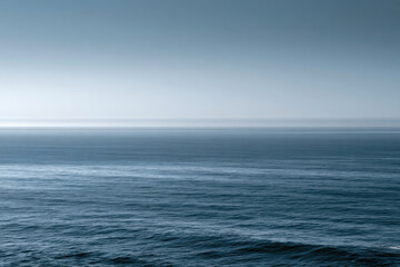 Fototapeta premium The soft blue hues of a misty ocean horizon create a tranquil and dreamy atmosphere, inviting viewers to reflect on the vastness and beauty of the sea at dawn.