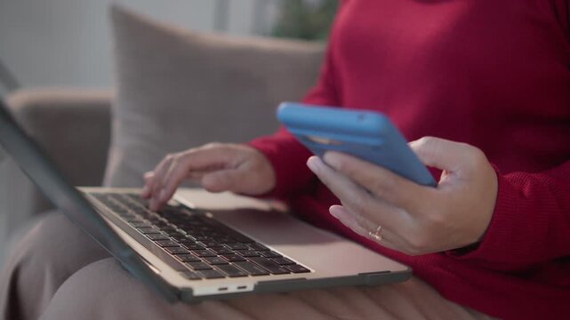Muslim woman in a hijab using a laptop and smartphone on a living room sofa to complete two-factor authentication, capturing cybersecurity, secure account access, and online verification.