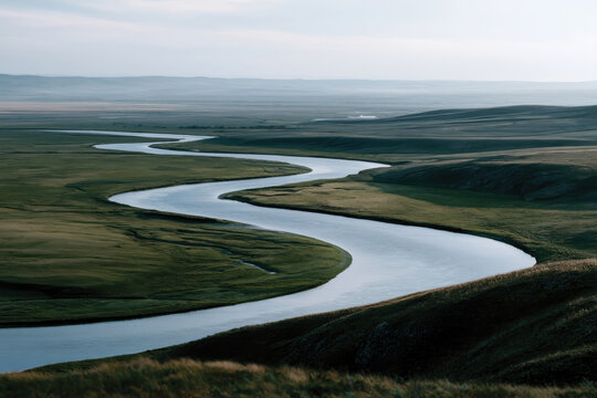 A curvy river gracefully flows through an expansive green landscape, showcasing nature's beauty and inviting viewers to reflect on tranquility and the wonders of the natural world.
