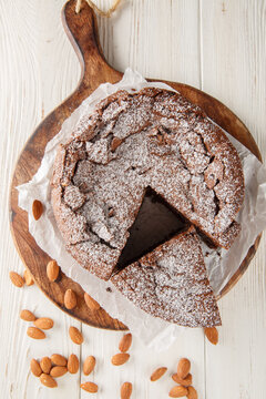 Torta Caprese Italian Flourless chocolate Cake closeup on the wooden board on the table. Vertical top view from above