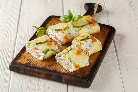baked zucchini roll with cheese, stuffed with salmon and cream cheese, on a wooden board on the table. Horizontal