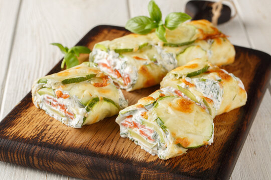 Appetizer Roll of sliced ​​zucchini stuffed with salmon and cream cheese close-up on a wooden board on the table. Horizontal