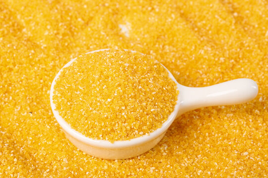 Yellow corn grits polenta in wooden spoon on golden background - healthy cooking ingredient