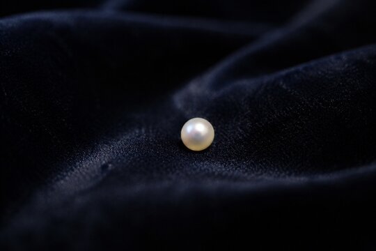 A tiny pearl on dark velvet fabric, soft light highlighting its gentle luster.