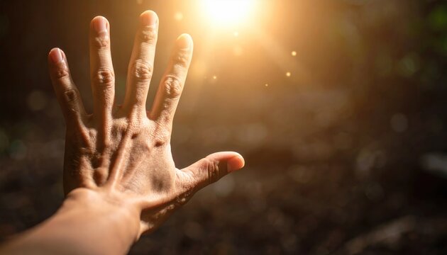 Human hand reaching towards bright, golden sunlight, symbolizing hope, spirituality, and divine connection.