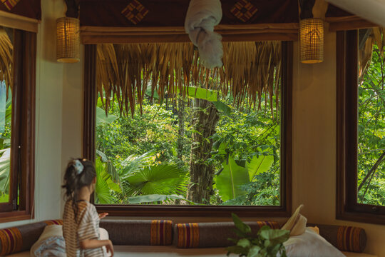 Girl gazing out thatched window at lush jungle greenery, Pu Luong, Vietnam