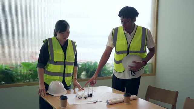 Engineers planning renewable energy project with eco house models and wind turbines.	