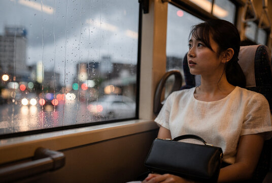 Young Woman Looking Out of Rainy Bus Window at Night