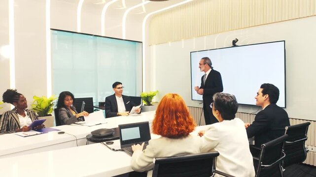 A diverse team in a modern conference room listens to a presenter at a digital whiteboard during a corporate meeting.