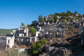 Fototapeta premium Ruined stone houses on a steep rocky hillside under a clear blue sky in the abandoned ghost town of Kayakoy, Fethiy, Turkey, November 11, 2024