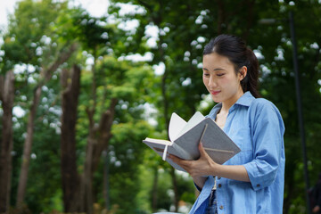 Fototapeta premium Education, university and woman in campus, Young asian woman smiles widely while tacking note. She standing in campus with her ready. Enjoying education outdoors with textbook