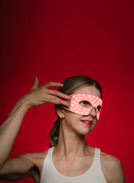 Red light therapy eye mask. smiling woman profile wearing infrared light therapy mask. touching the mask with her fit hand. dark background