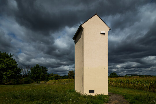 Small rural electrical transformer station beneath dramatic storm clouds in the German countryside, surrounded by grassland under changing weather conditions