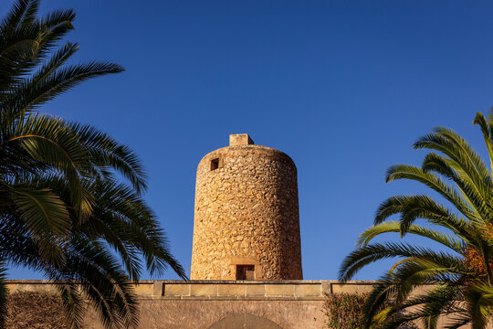 Historic stone tower framed by palm trees against a clear blue sky, highlighting traditional Mediterranean architecture and cultural heritage in Spain.