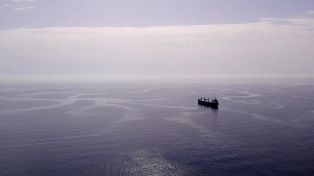 Cargo ship sailing in open water on the calm Mediterranean sea, creating surreal patterns with its wake