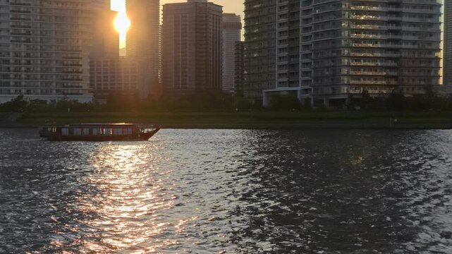 ビルの間に沈む夕陽と船が見える都市の風景。