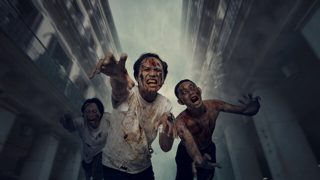 A group of terrifying, blood-covered zombies with angry faces chasing and reaching out towards the camera in a dark, foggy apocalyptic city street during Halloween