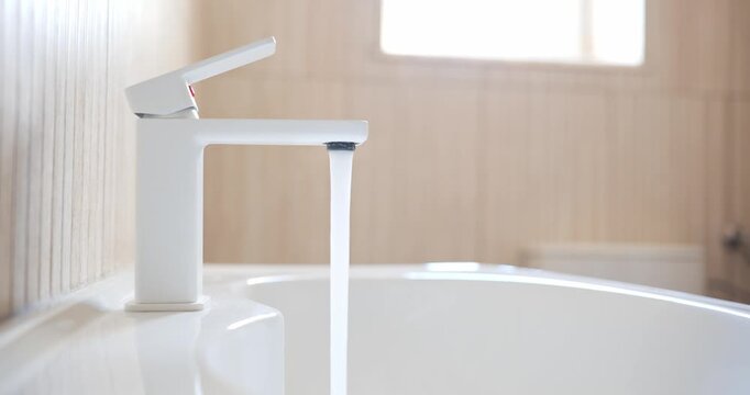Hand opening and closing white modern bathroom faucet turned on and off running water stream.