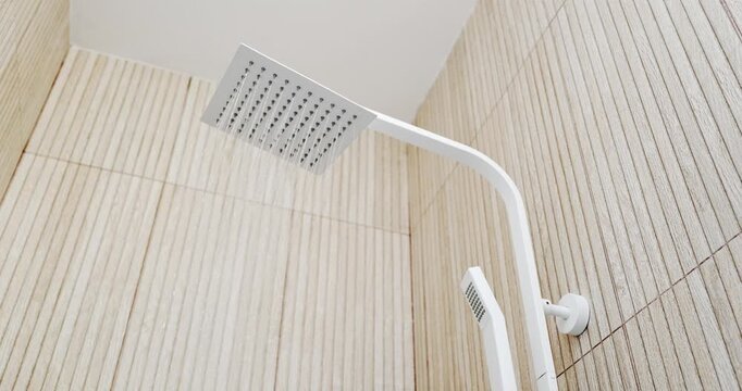 Video of a modern white square rain shower head with water flowing on a slatted wood tile wall.