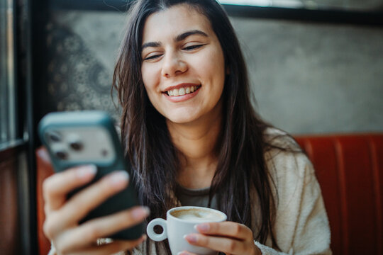 Young woman smiling while looking at smartphone in cafe