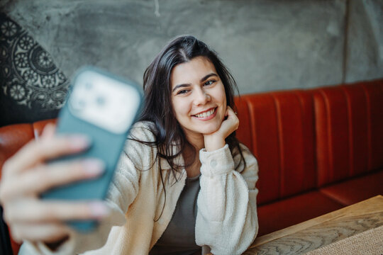 Young woman taking selfie with smartphone in cafe