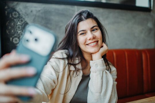 Young woman taking selfie while smiling in cafe