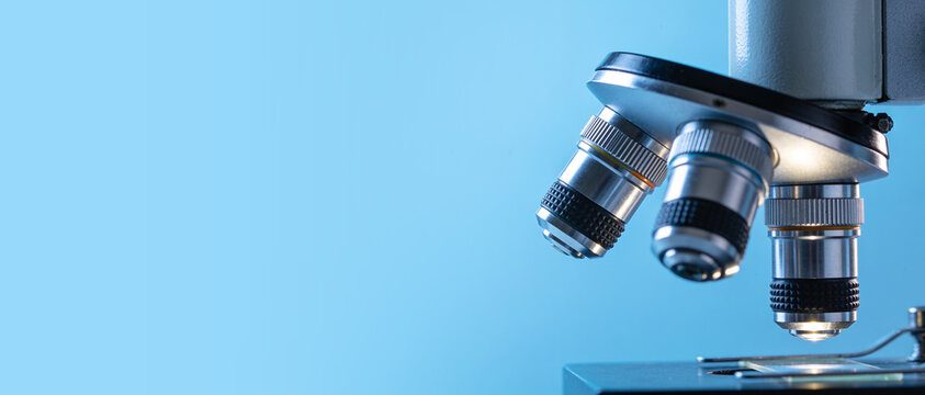 Close-up of a microscope objective lens turret isolated on a solid light blue background.
