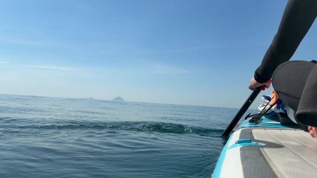 Person rowing a paddleboard on calm open sea with distant islands under a clear sky. Mindful movement.