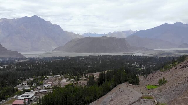 Panoramic drone shot of a green valley settlement surrounded by high peaks in Chitral Pakistan