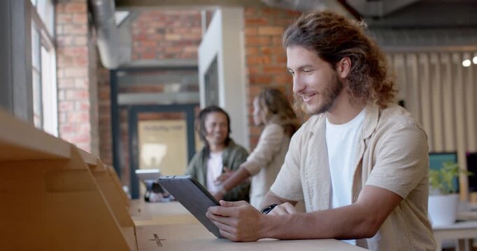Adult man tapping tablet, gesturing and speaking at long wooden counter by windows, sharing content