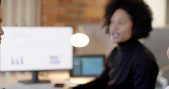 Diverse team reacting to update at desk, African American woman explaining data, pointing to screen
