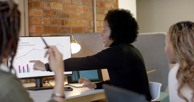 African American desk team watching woman in black top pointing at monitor trend and seeking input