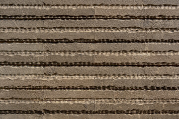 Textured brown stone wall cladding with horizontal chiseled ribbed pattern background. © Okta