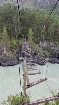 Scenic view of the famous broken wooden suspension footbridge in the Che-Chkish area, hanging dangerously over the fast turquoise Katun river in the Altai mountains