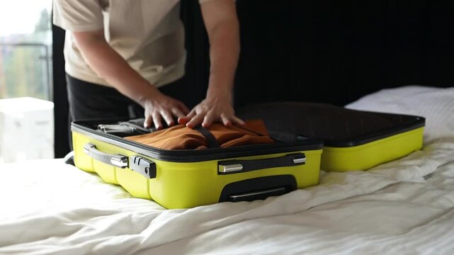 Close up of male hands carefully unzipping and opening a bright yellow hard-shell suitcase on a white bed. Unpacking clothes and baggage after vacation, arriving at a hotel room, or returning home