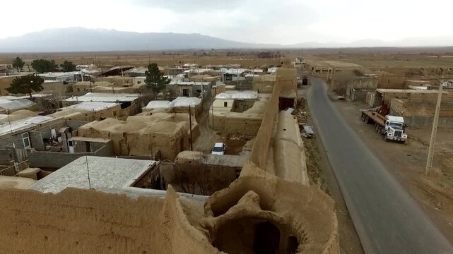 Beautiful wide aerial perspective tracking an old clay castle fortification built in a remote desert village oasis, showcasing ancient mud brick walls and traditional heritage style.