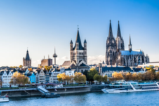 Cologne, Germany - October 26, 2011: The twin spires of Cologne Cathedral rise above the old town skyline, with river cruise boats docked along the Rhine.