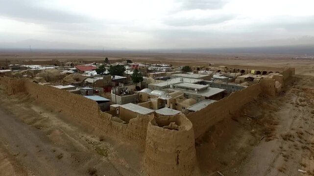 Beautiful wide aerial tracking shot over an ancient clay castle fort compound built in a remote desert village settlement, showcasing traditional mud brick architecture and heritage style.