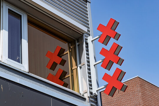 Amsterdam, Netherlands, May 23, 2026. The iconic three red crosses of the Amsterdam coat of arms mounted on a modern grey office building with a reflection visible in the window pane.