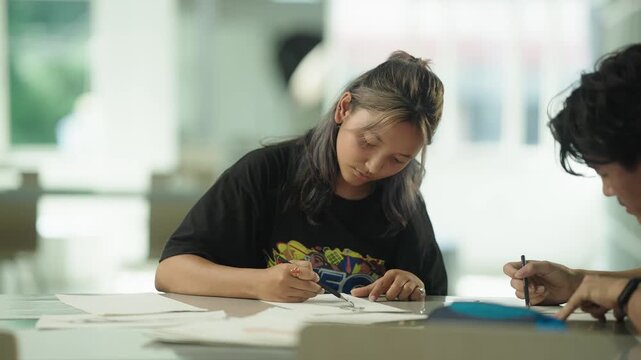 Fashion design student and classmate engaged in a friendly conversation about a sketch design while sitting close together at library table
