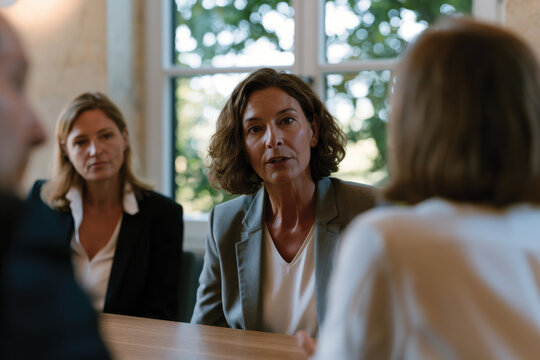A confident businesswoman addressing a group during a meeting with an assertive tone, ready to lead discussions on critical business strategies and opportunities in a modern office space.