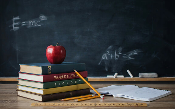 Physics classroom equation E=mc&sup2; on chalkboard with apple and books. Educational science concept featuring relativity formula, textbook stack, and...