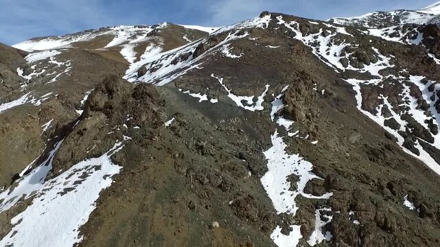Spectacular high angle drone overview tracking along a jagged mountain ridge with melting winter snow patches, showcasing rugged topography and textured geological structures from uav.