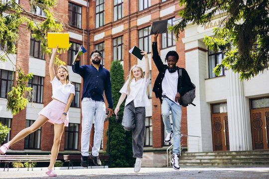 Excited diverse students jumping together in front of a university building, celebrating academic achievement and a bright future