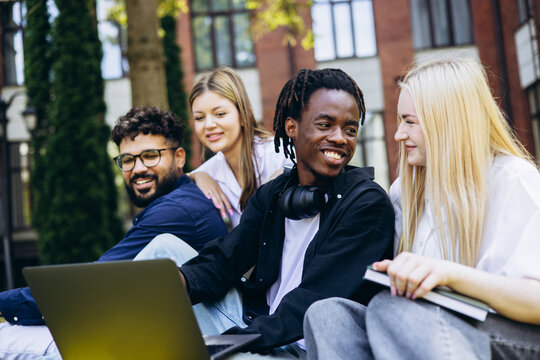 Group of happy multiracial college students using a laptop for learning and teamwork outdoors on campus