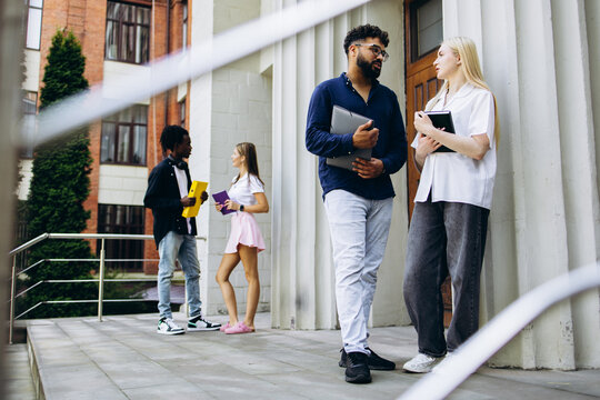 Group of diverse university students standing and talking on campus, holding books and laptops, reflecting learning and dialogue